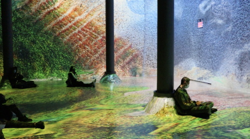 People relaxing in an immersive digital art installation with nature projections covering walls and floor